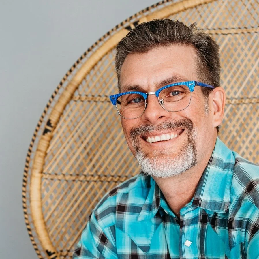 Scott Dory, smiling, wearing blue glasses and a plaid shirt